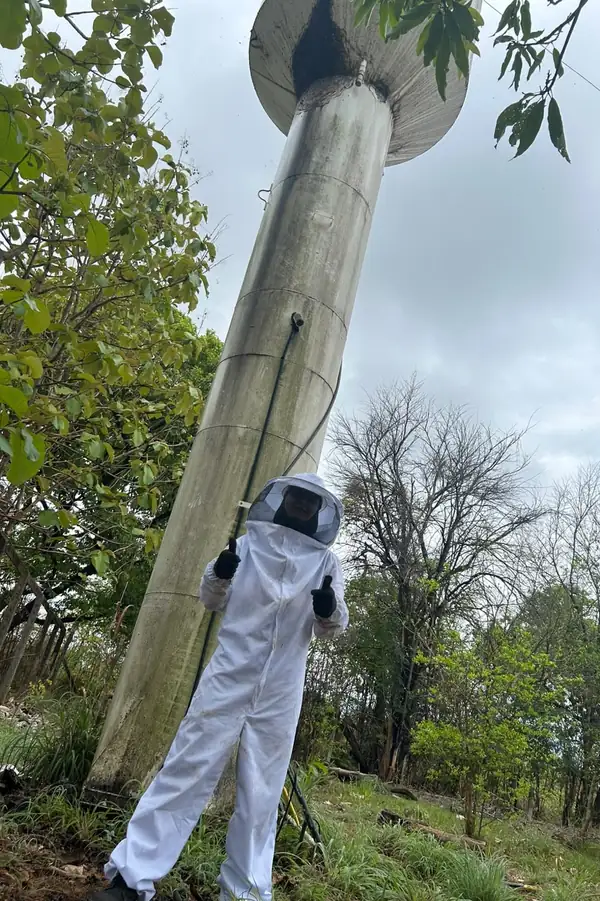 Técnico da Zero Pragas Goiânia com roupa de apicultor ao pé de uma caixa d'água, depois de retirar o enxame